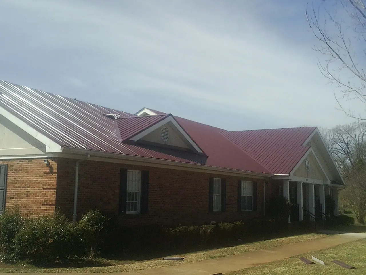Red metal roof with gabled entries on a long brick building, from a Hail Damage Roof Repair job in Moorestown