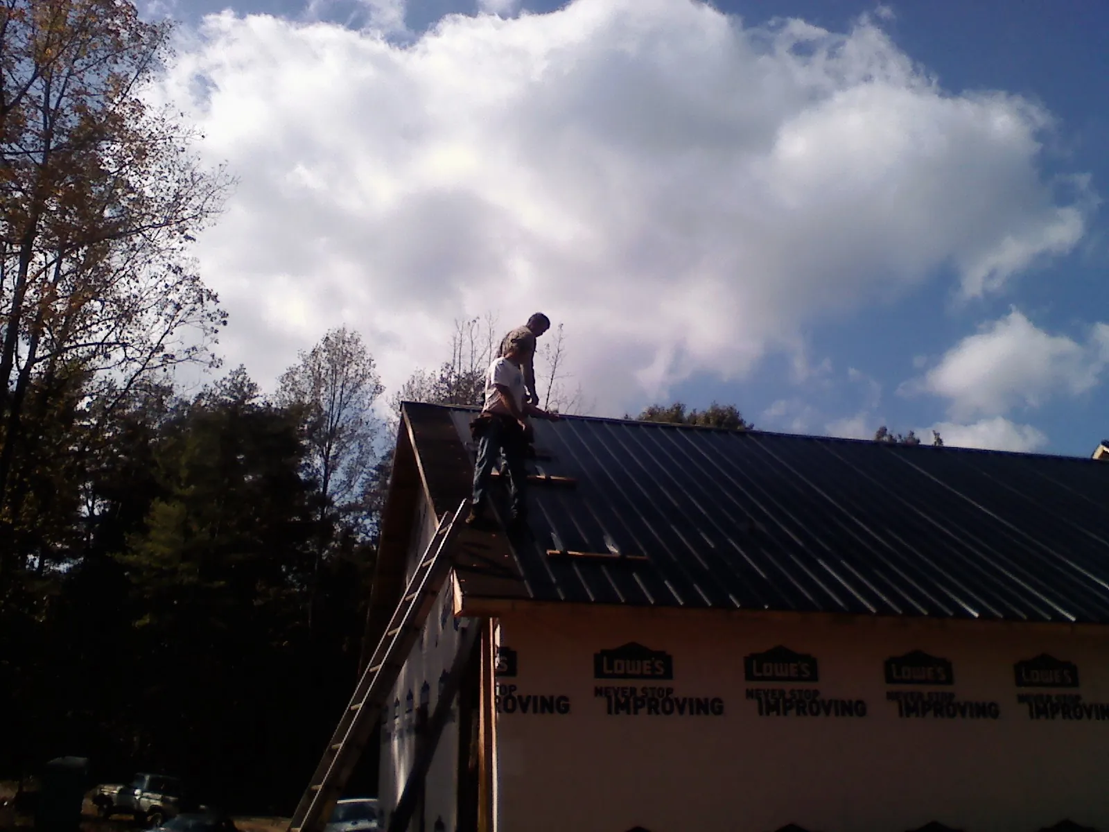 Roofer fastening dark metal panels high against a cloudy sky, from a Roof Inspection job in Moorestown