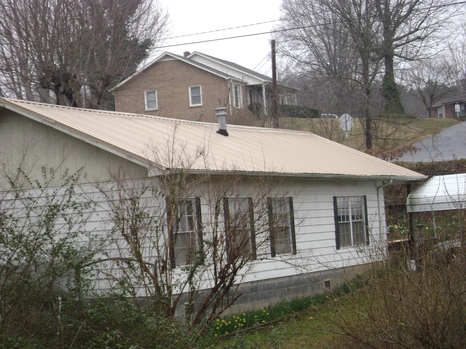 Tan metal roof on a white sided house set into a hillside — Commercial Roofing by Roofing Brothers in Moorestown